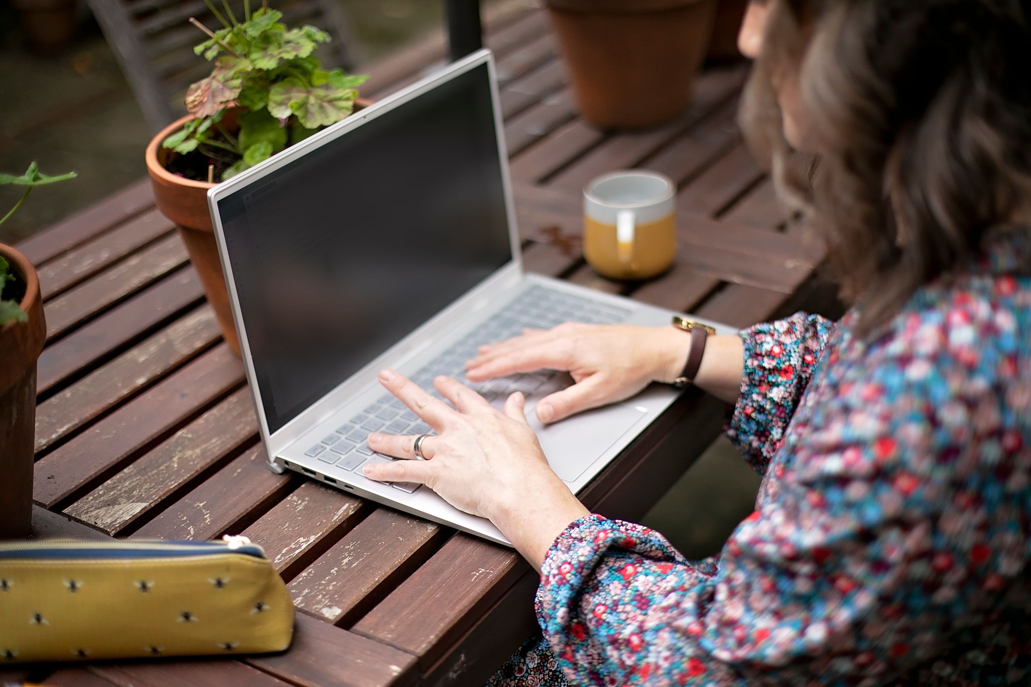 Image of Hannah from the side working on a laptop, she is outside working on a garden table